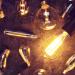 Vintage old light bulb glowing yellow on rough dark background surrounded by burnt out bulbs. Idea, creativity concept.