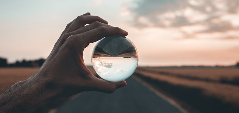 man holding crystal ball over a road at sunset
