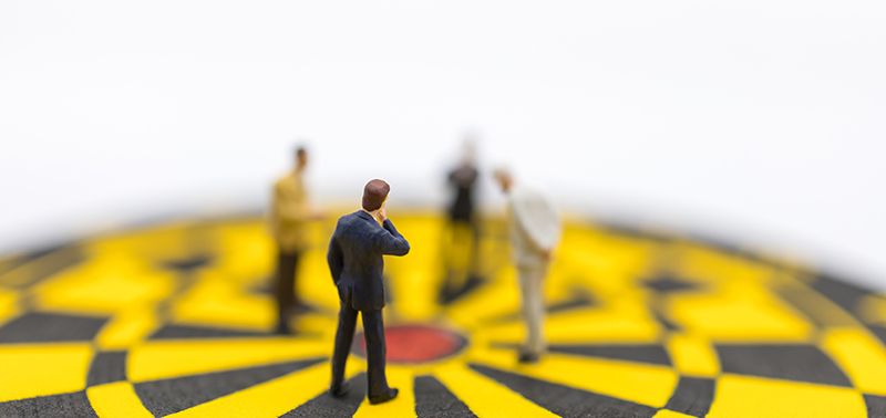 Business, Planning, Succession and Management Concept. Close up of group of businessman miniature figure standing and looking to center of yellow and black dart board on white background.