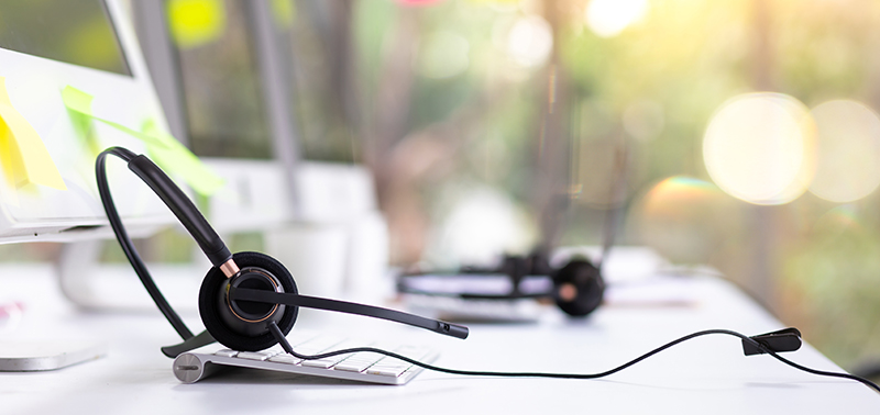 VOIP headset on desk with computer desktop at customer service and marketing support workplace. Office supplies of customer service. Communication support, call center and helpline concept.