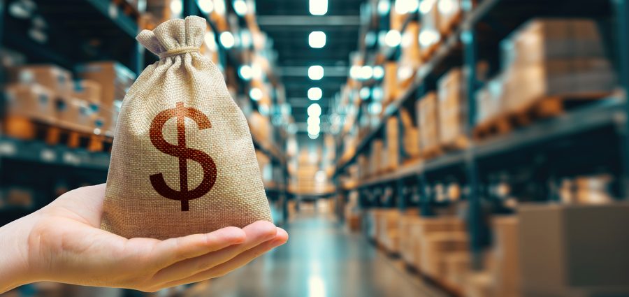Trade in goods and production. Profit from trading. Import and export. Warehousing logistics. Delivering. Money bag on background of modern distribution warehouse or shipping warehouse. Blurred