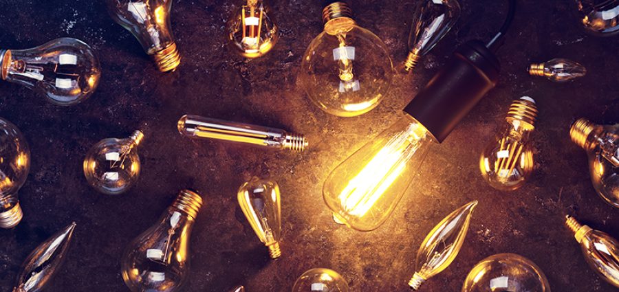 Vintage old light bulb glowing yellow on rough dark background surrounded by burnt out bulbs. Idea, creativity concept.