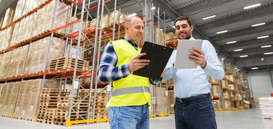 wholesale, logistic business and people concept - warehouse worker and businessman with clipboard and tablet pc computer