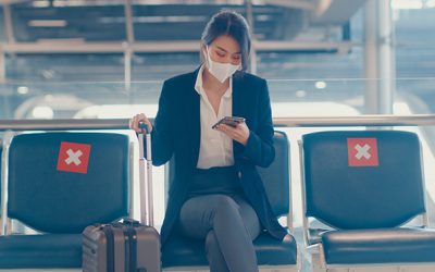 business lady traveller wear suit sitting with suitcase and use smart phone chat message in bench wait for flight at airport. Business travel commuter in covid pandemic, Business travel concept.