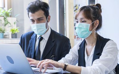 man and woman wearing masks working on a laptop together